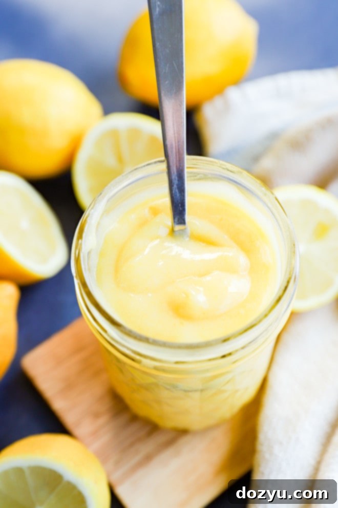 Effortless Zesty Lemon Curd 5 A mason jar of creamy, smooth lemon curd with a spoon in it, surrounded by fresh lemons and berries, indicating a delicious breakfast or dessert topping.