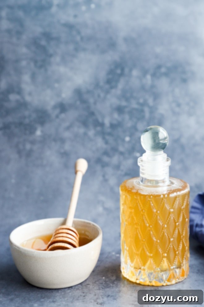 honey simple syrup in a bottle with a bowl of honey, ready for use in various recipes