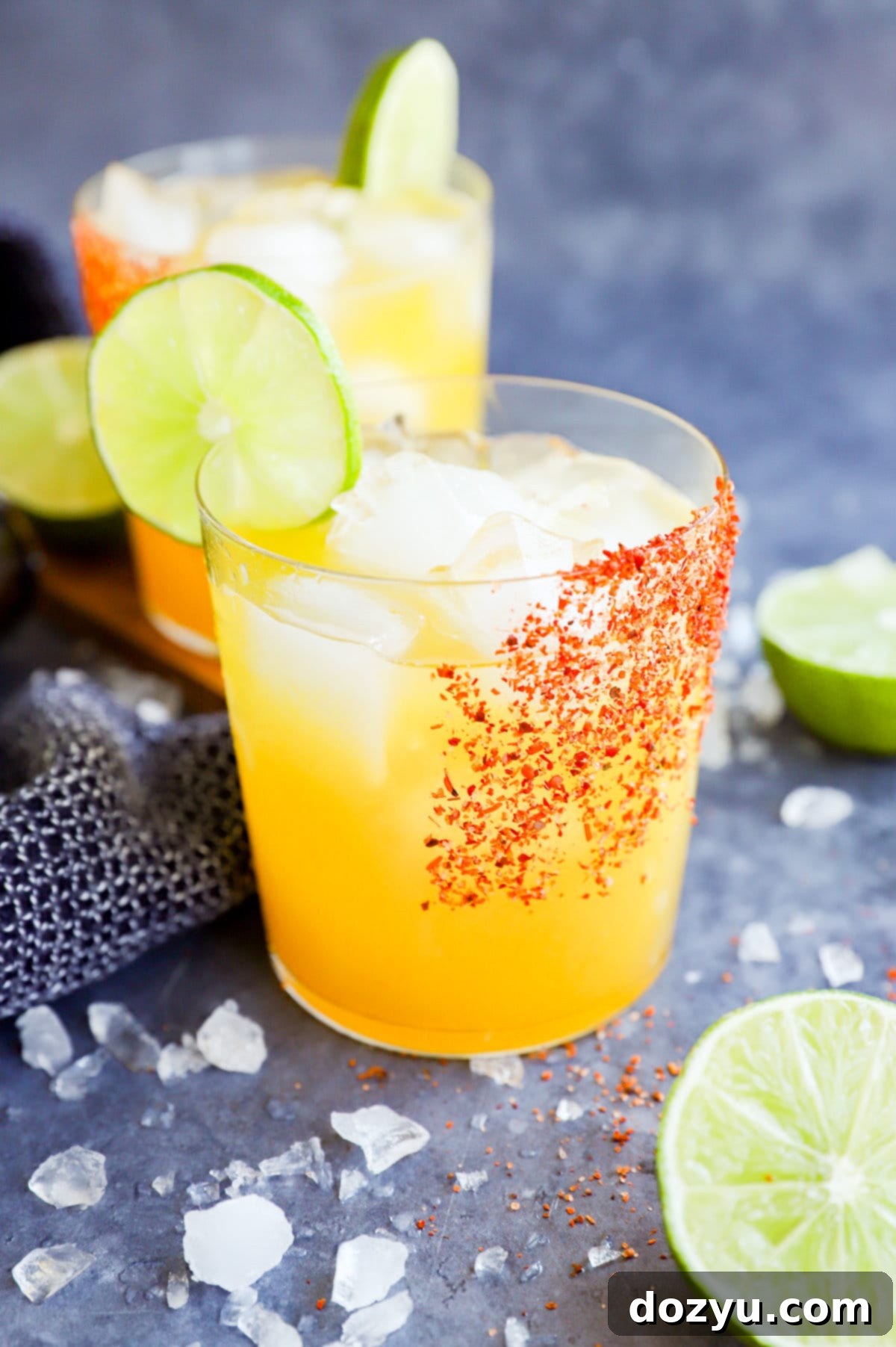 Two glasses of vibrant orange passion fruit margaritas on a table with a lime slice garnish.