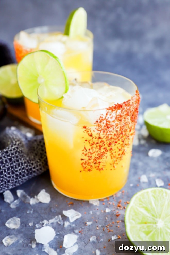 Two glasses of vibrant orange passion fruit margaritas on a table with a lime slice garnish.