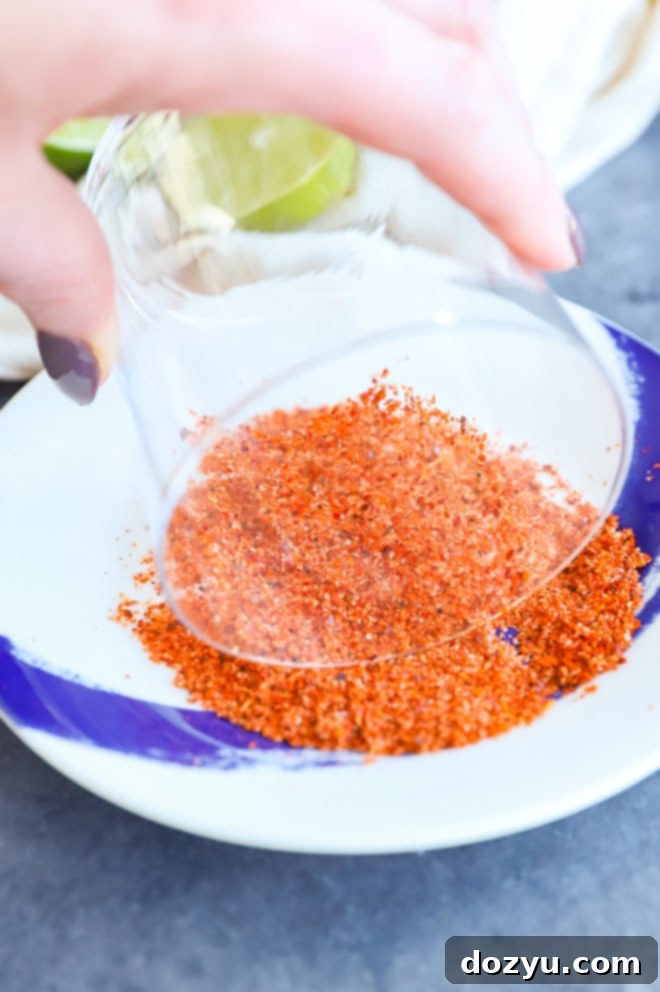 A hand rimming a cocktail glass with Tajin seasoning on a plate, preparing for a passion fruit margarita.