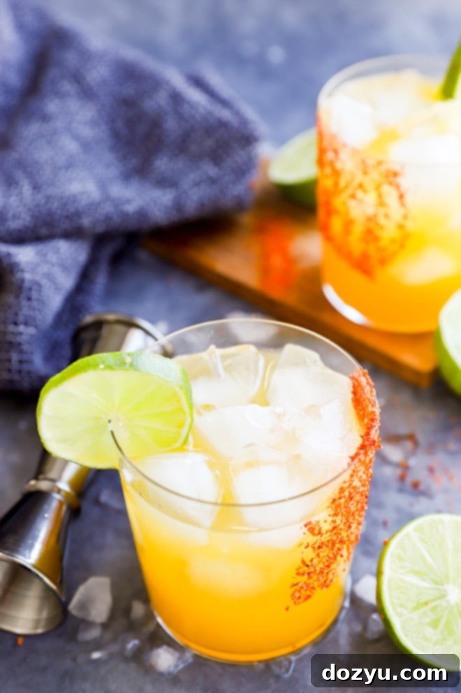 A close-up of a passion fruit margarita in a glass rimmed with Tajin, garnished with a lime wheel and a jigger in the soft background.