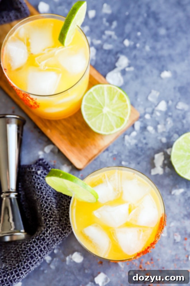 Glasses of passion fruit margaritas surrounded by ice, with lime garnishes and a jigger in the background.