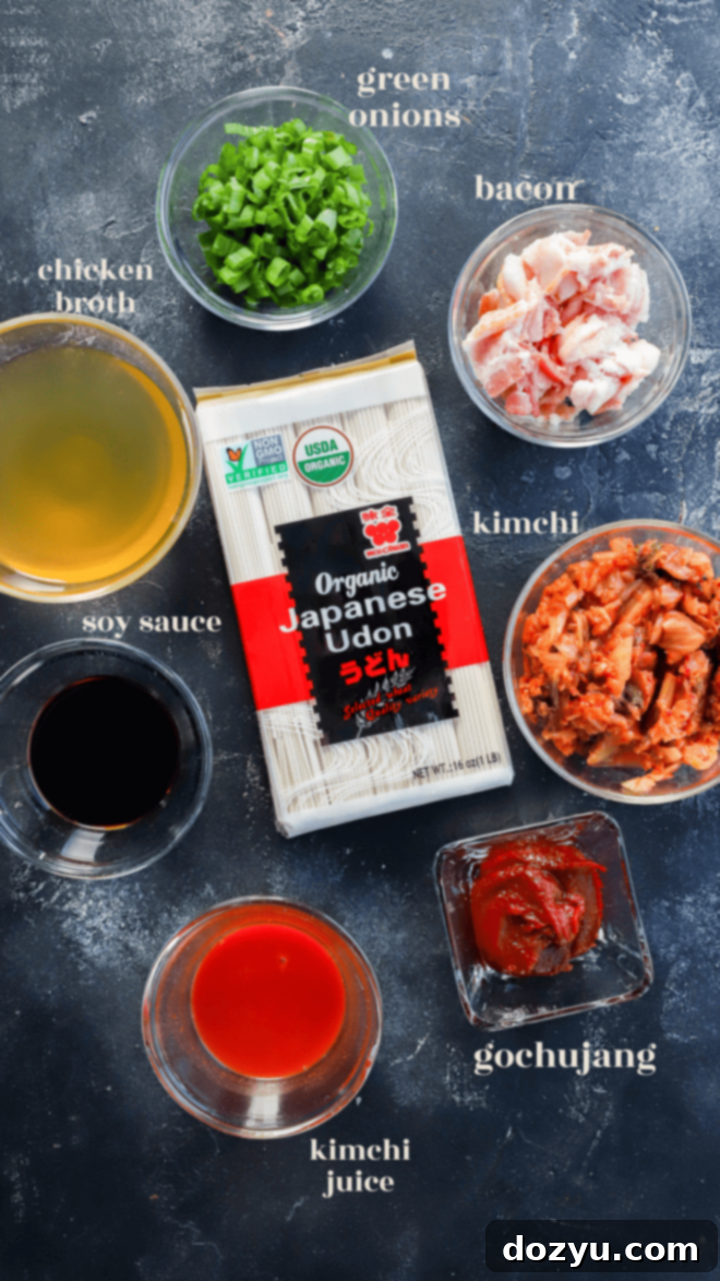 A collection of ingredients laid out for making kimchi udon, including bacon, kimchi, udon noodles, broth, soy sauce, gochujang, and scallions.