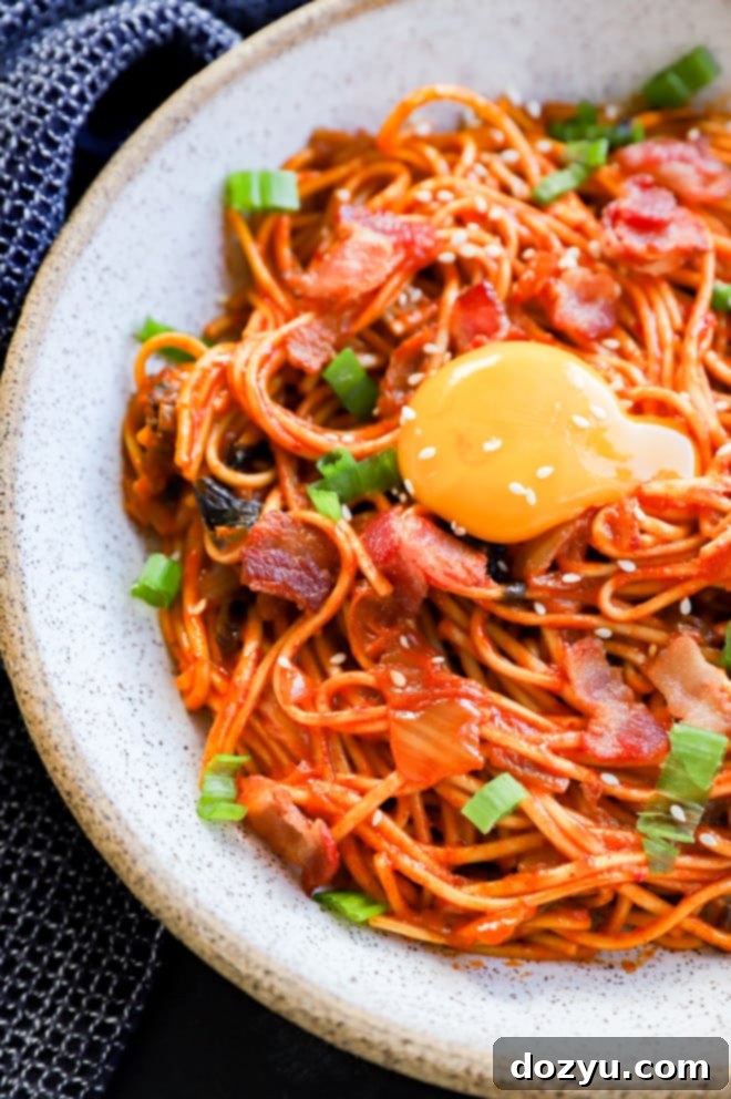 Close-up of a runny egg yolk being broken over spicy kimchi noodles in a bowl