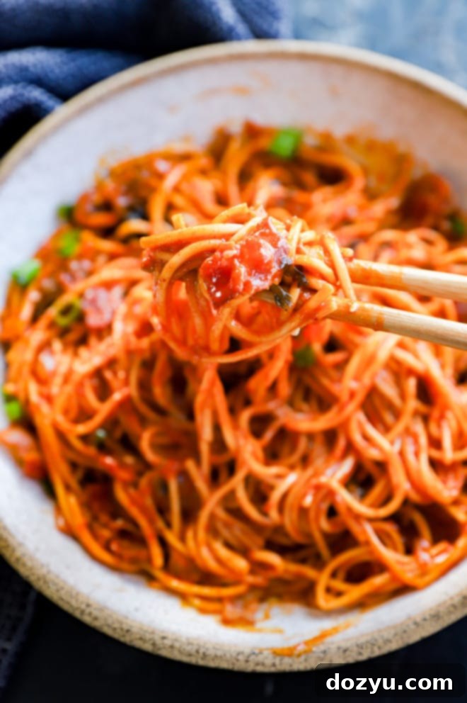 Chopsticks lifting spicy, creamy noodles from a bowl, showcasing the rich sauce and udon texture