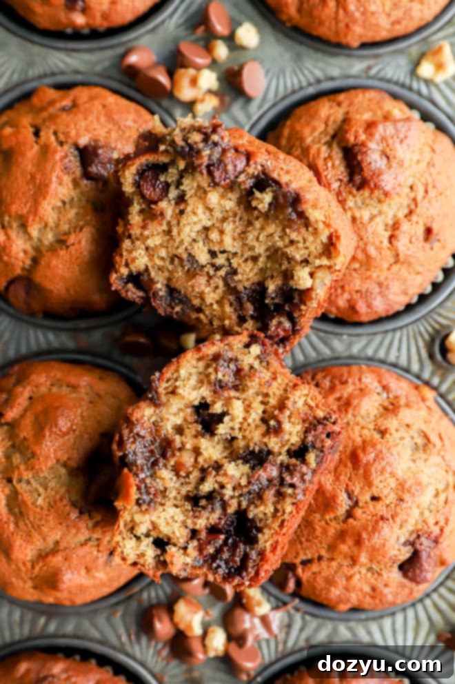 A banana bread muffin cut in half, revealing a moist interior with scattered chocolate chips and walnuts.