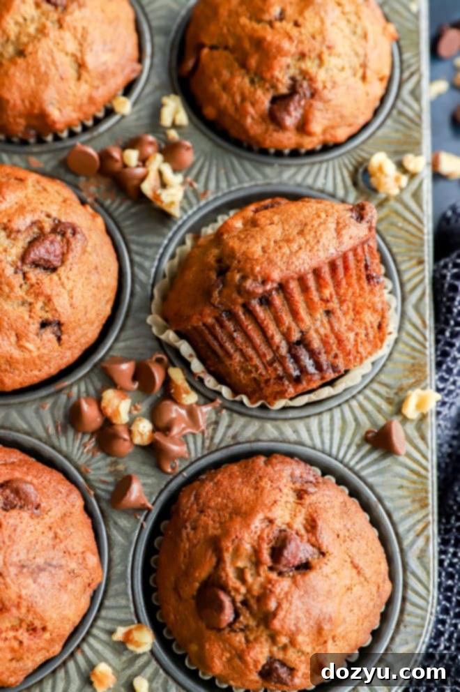 A tray of freshly baked banana bread muffins, with one muffin playfully laid on its side, showing its golden-brown exterior.