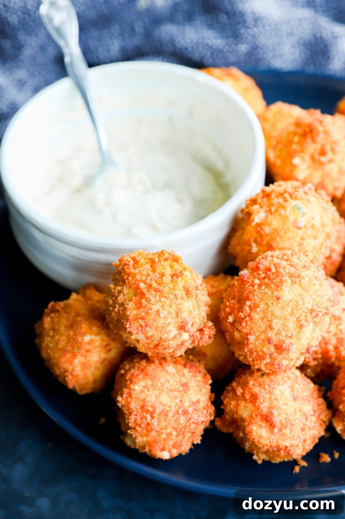 A vibrant close-up shot of crispy, golden-brown potato cheese balls artfully arranged on a white plate, accompanied by a small bowl of creamy dipping sauce.