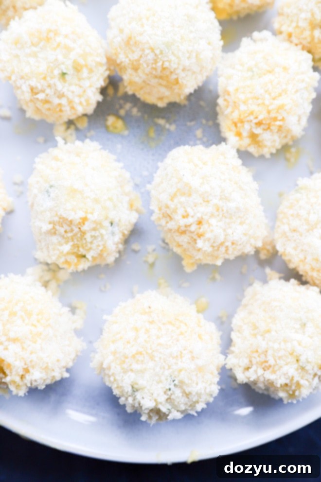 Hands carefully coating formed potato cheese balls with a generous layer of panko breadcrumbs in a bowl, preparing them for frying.