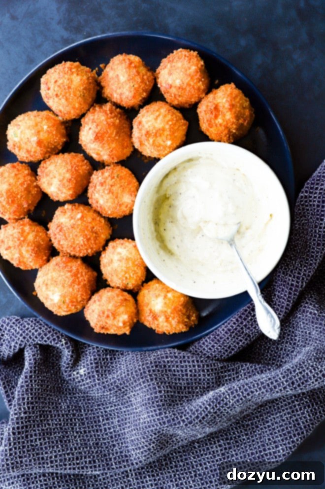A beautifully arranged plate of crispy, golden-fried potato cheese balls, served alongside a creamy roasted garlic aioli for dipping.
