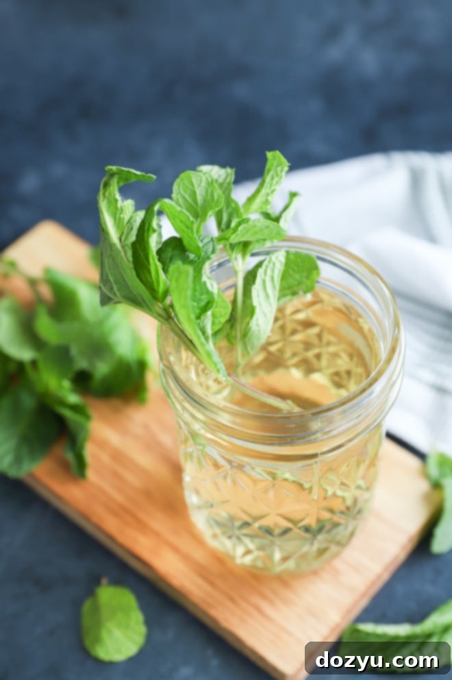 Fresh mint in a cup of mint simple syrup with mint leaves all around and cutting board