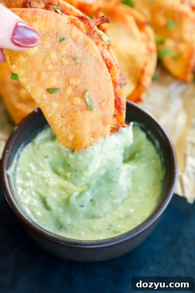 A crispy chicken taco being dipped into the avocado tomatillo sauce