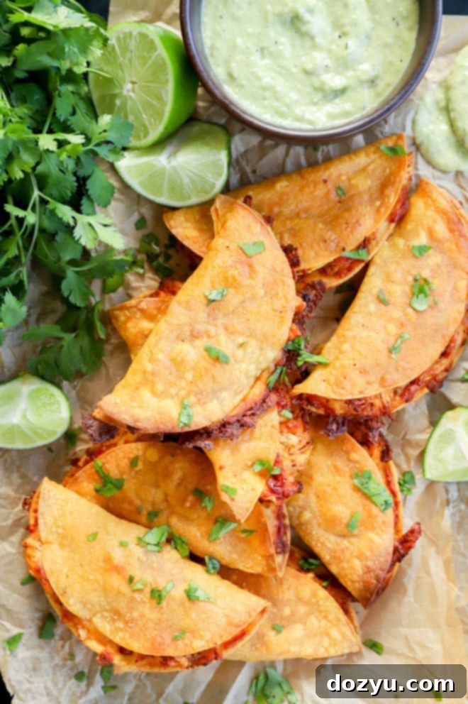 A pile of baked chicken tacos on parchment paper, ready to be served with avocado tomatillo sauce