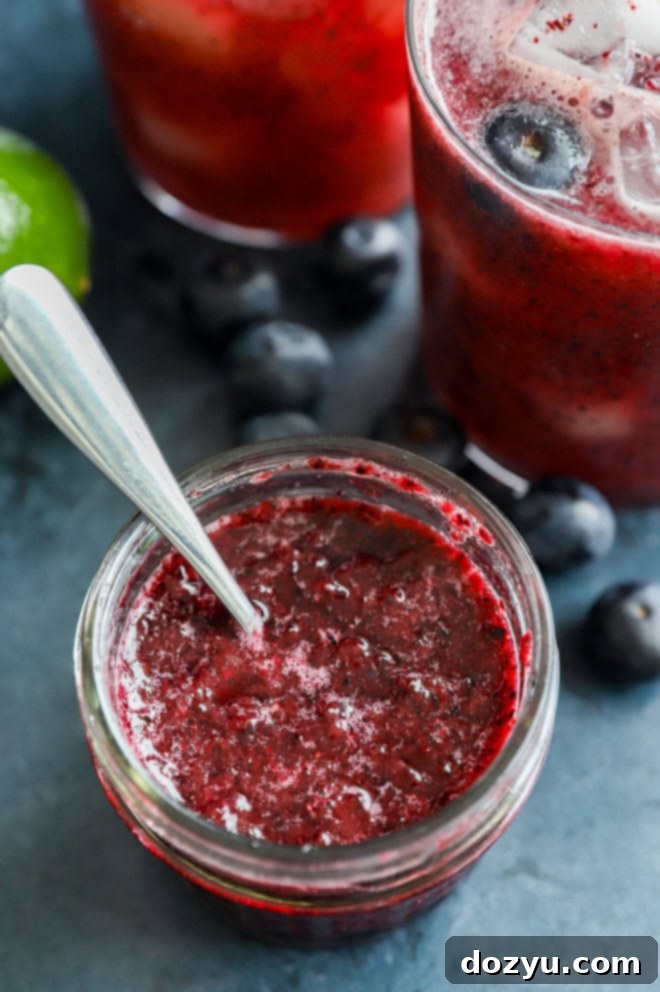 Homemade blueberry sauce stored in a small mason jar, ready for making delicious cocktails.