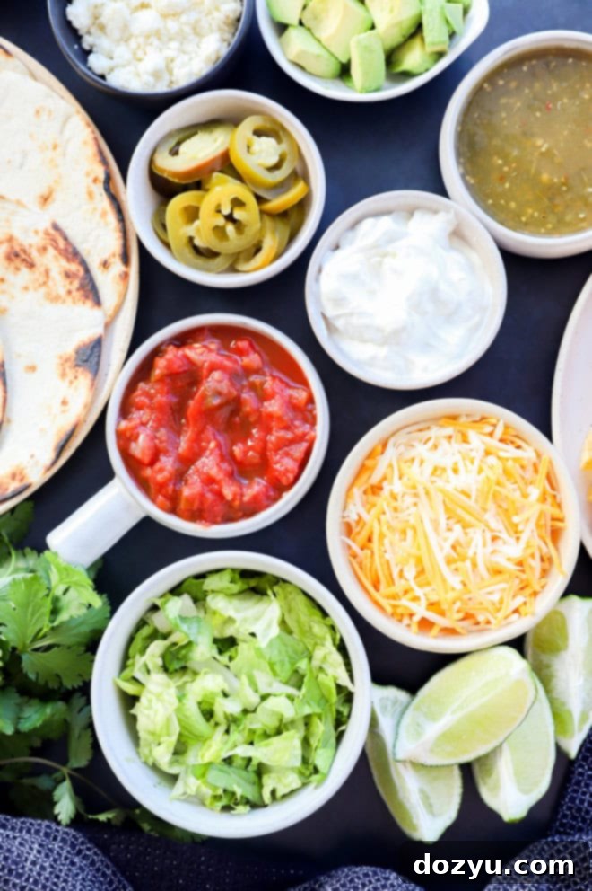 Image of a variety of vibrant taco toppings including shredded lettuce, fresh lime wedges, shredded cheese, creamy sour cream, zesty salsa verde, rich salsa, spicy pickled jalapeno slices, and warm tortillas