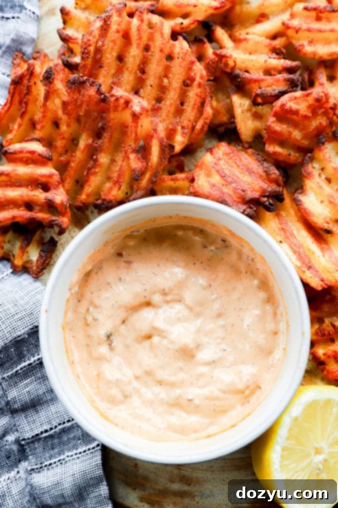 Image of a dipping sauce with fried potatoes and a lemon half on a platter with a linen napkin