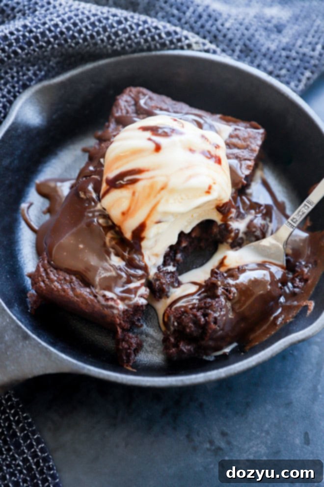 A fork taking a spoonful of melting ice cream and fudgy brownie from a sizzling skillet sundae.