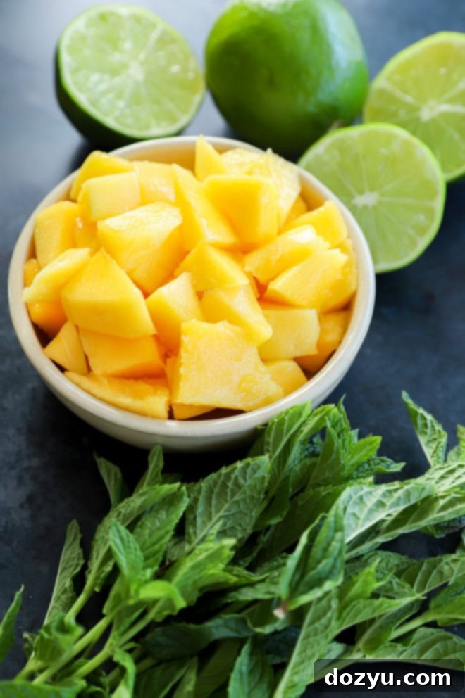 Tropical Mango Mojito 3 Freshly cut mango pieces in a bowl, surrounded by whole limes and vibrant mint leaves, showcasing the key ingredients.