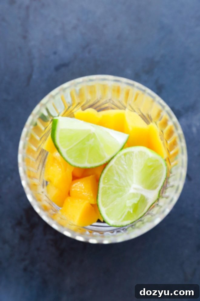 Tropical Mango Mojito 4 Mango chunks and lime wedges are placed in a cocktail glass, ready to be muddled together, showing the initial step of the recipe.
