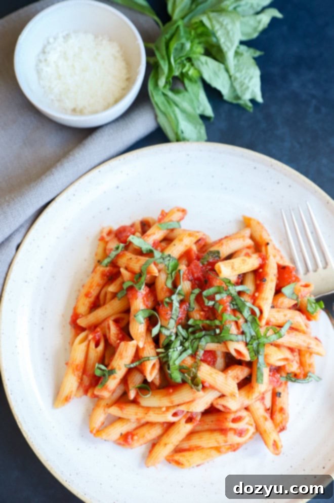 Penne pomodoro on plate with fork, fresh basil on top and grated parmesan