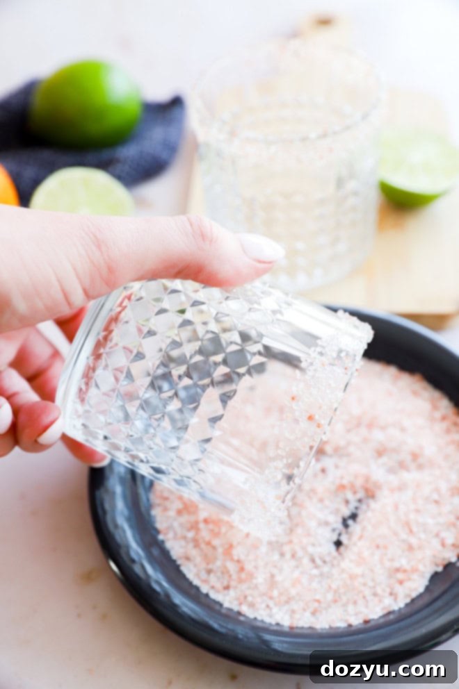 Close-up of a hand rimming a cocktail glass with salt, preparing it for a Patron margarita