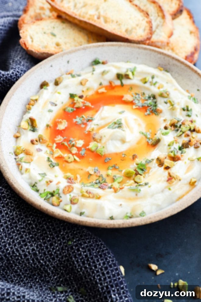 Whipped ricotta in a bowl adorned with hot honey, crunchy nuts, and fragrant fresh herbs – a vibrant and inviting appetizer.