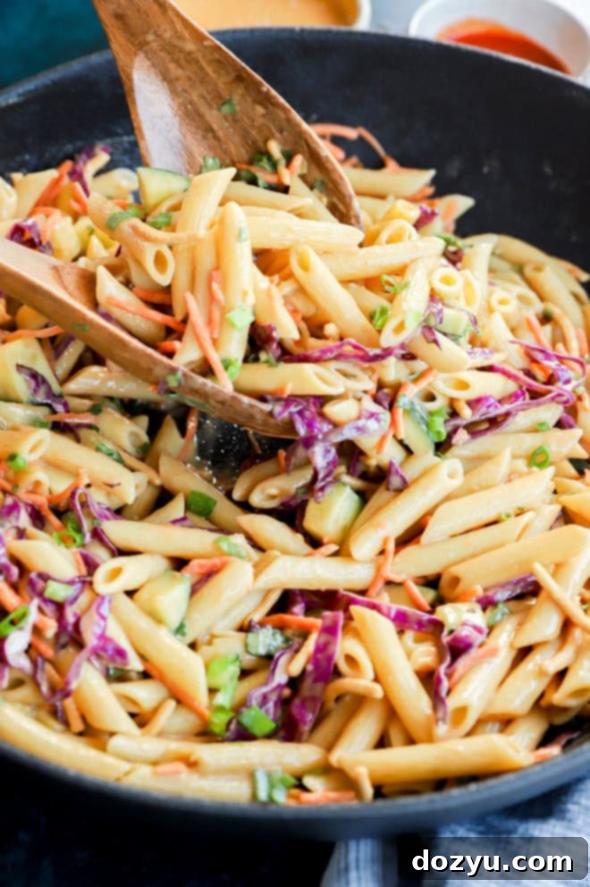 lifting pasta salad out of a serving bowl with woodn spoons