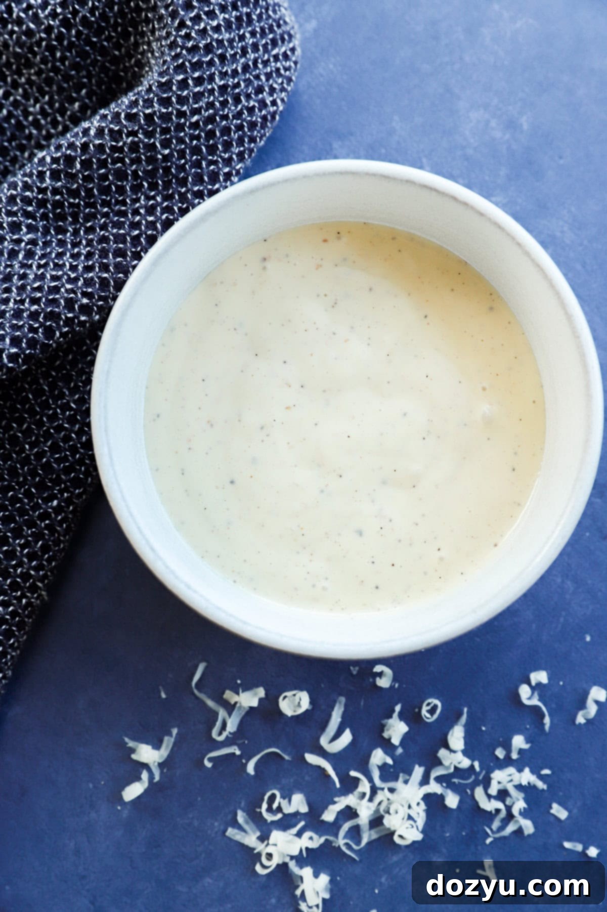 homemade caesar salad dressing in a bowl with grated parmesan cheese on the side