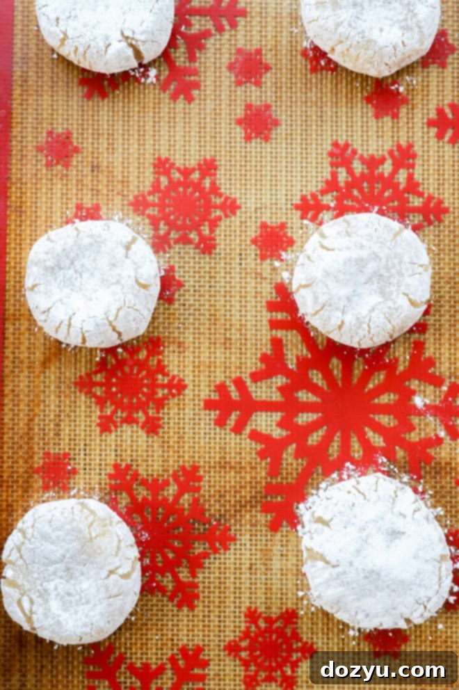 raw amaretti biscuits on lined baking sheet rolls in powdered sugar