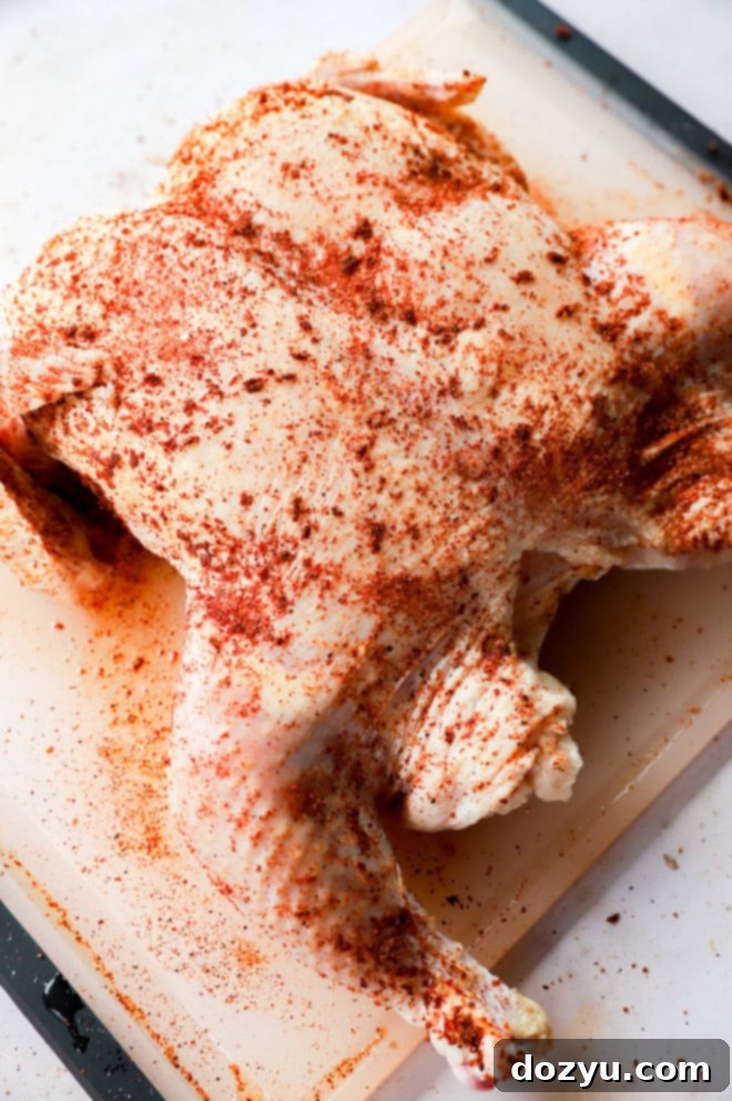 whole raw chicken with seasoning all over on cutting board