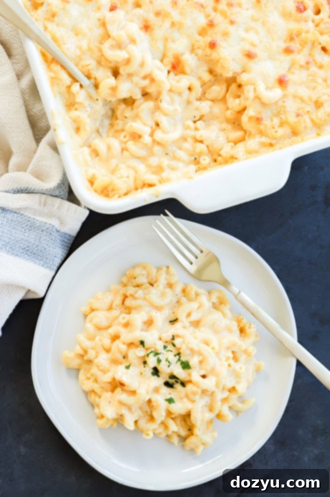 A serving of four cheese mac and cheese on a white plate next to the full casserole dish, ready to be enjoyed.