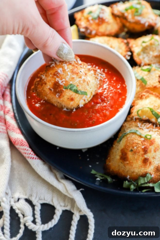 A hand dipping a crispy air fryer ravioli into a bowl of marinara sauce, garnished with fresh herbs.