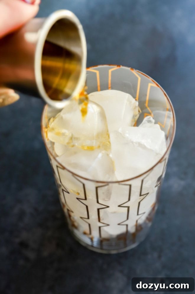 Pouring whiskey into a highball glass filled with ice