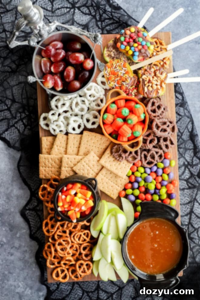 Overhead image of a vibrant Halloween dessert charcuterie board featuring an array of candies, fruits, and dips, all arranged on a spiderweb-patterned tablecloth.