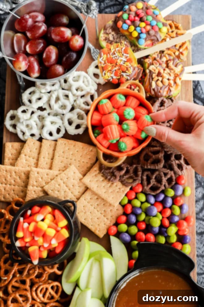 Hand reaching for a pumpkin-shaped candy from a festive pumpkin bowl, surrounded by other delightful Halloween treats on a dessert platter.