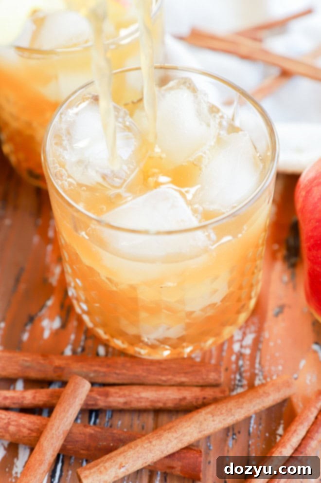 straining apple cider cocktail in cocktail glass filled with ice