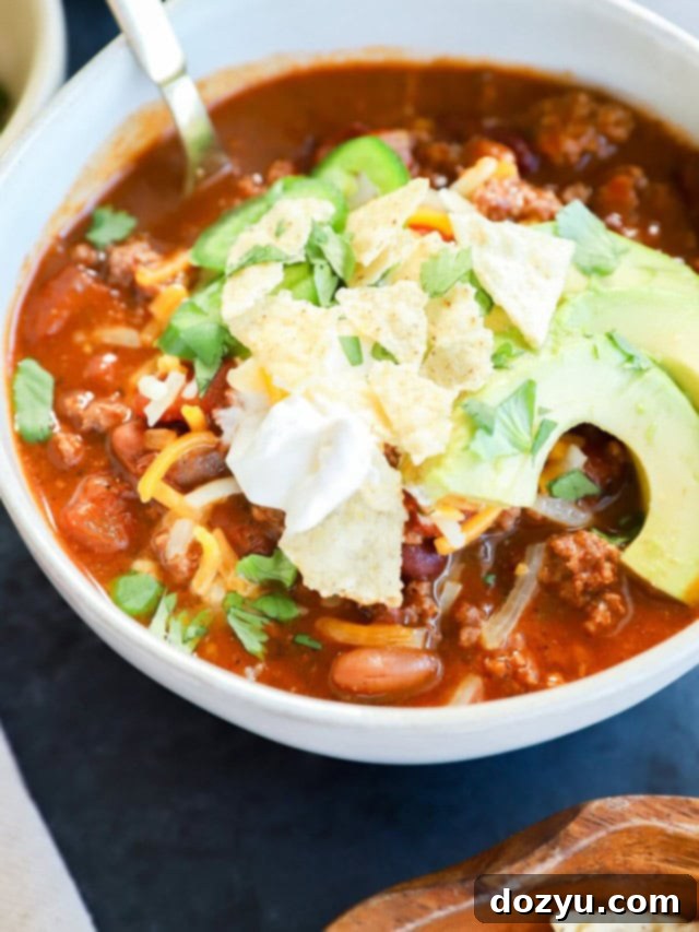 Make Your Own Chili Seasoning Mix 6 A steaming bowl of spicy taco chili, generously garnished with fresh avocado slices, a dollop of cool sour cream, and shredded cheese, creating a vibrant and appetizing presentation.
