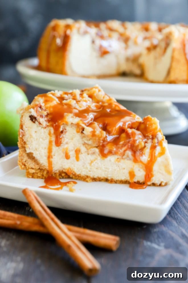 Slice of decadent caramel apple crumble cheesecake on a plate, garnished with fresh apple slices and cinnamon sticks, highlighting its creamy layers and crumbly topping.