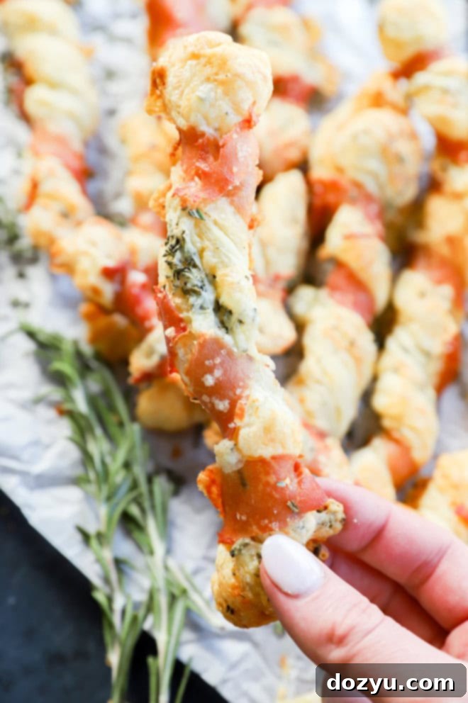 Flaky Prosciutto Cheese Twists 6 Hand holding prosciutto cheese twists over a pile of them with parchment paper