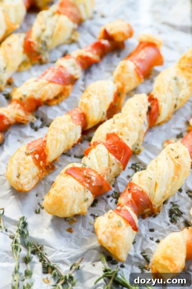 Flaky Prosciutto Cheese Twists 7 prosciutto cheese twists lined up on a piece of parchment paper with fresh herbs