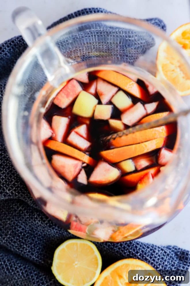 Ruby Red Sangria 5 stirring a fruity punch in a large pitcher with orange halves