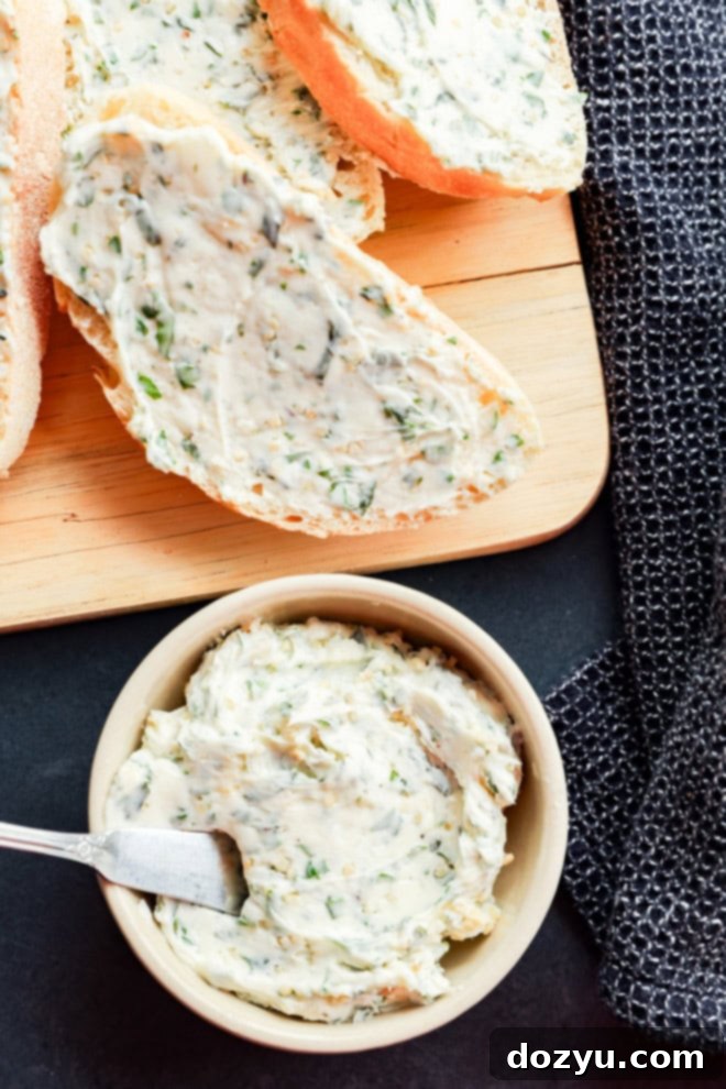 A bowl of homemade garlic herb butter with a spoon, next to sliced bread