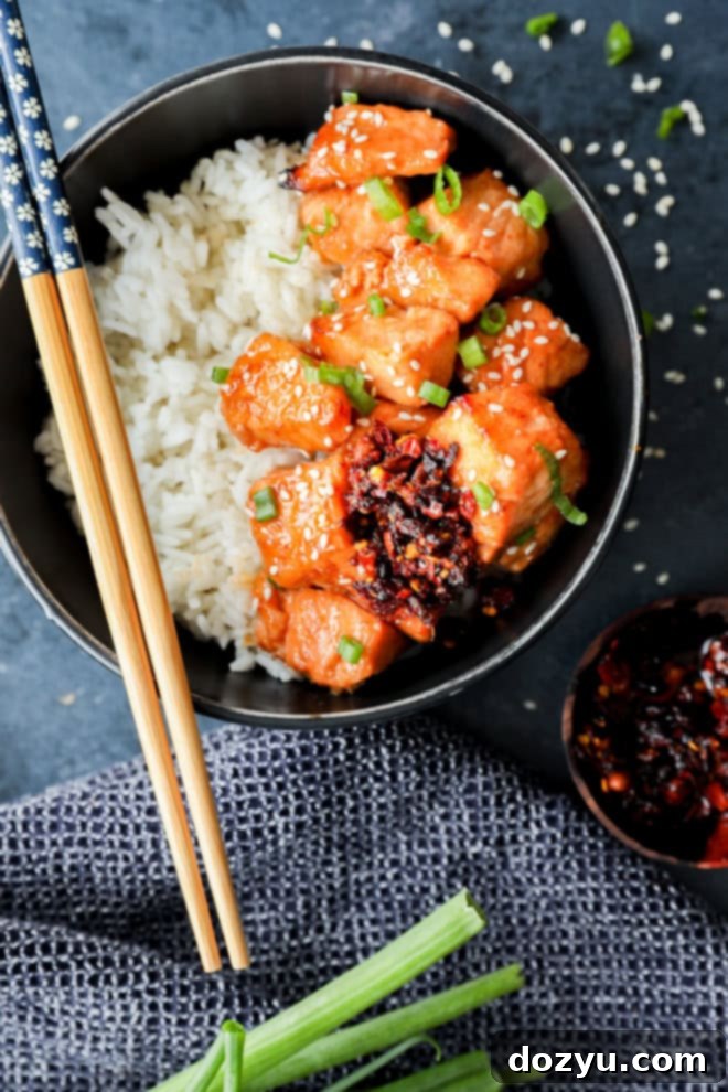 bowl of fish pieces in honey ginger glaze over rice in black bowl with chopsticks