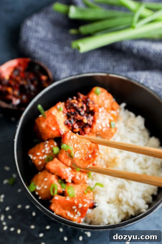 chopsticks holding a small piece of glazed salmon over salmon with rice