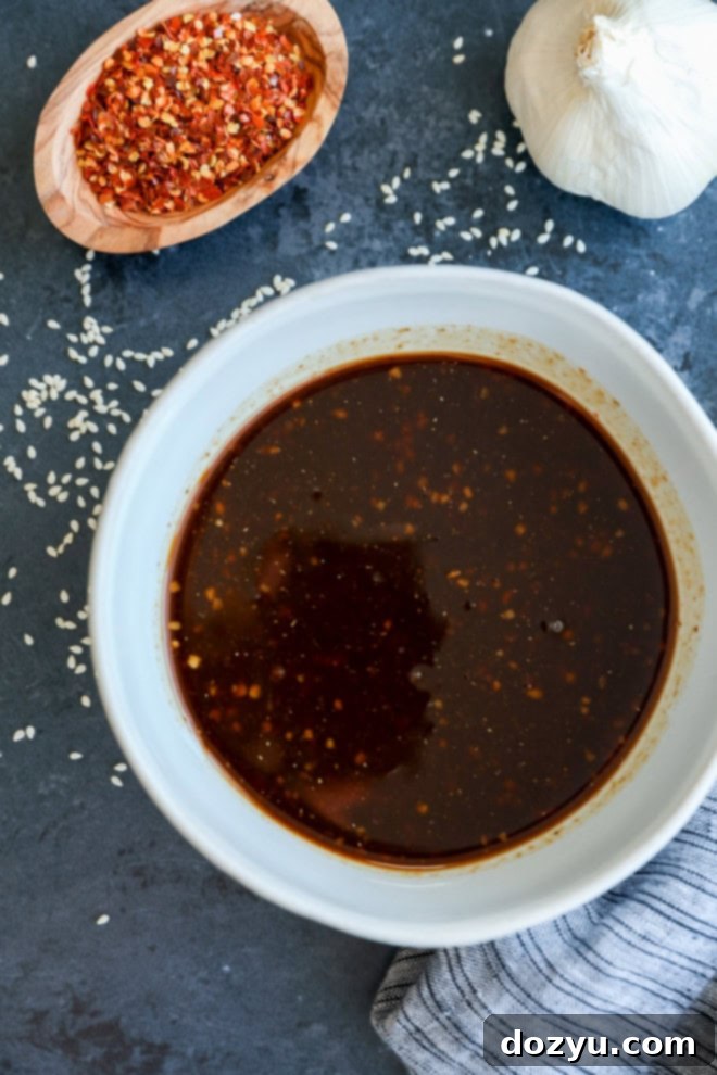Close-up of Asian pork belly marinade swirling in a bowl, highlighted by red pepper flakes and minced garlic, ready for pork.