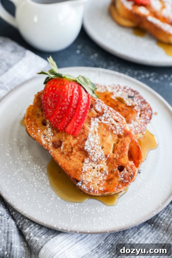 Sourdough French toast slices beautifully arranged on a white plate, garnished with a medley of fresh berries and a light dusting of powdered sugar, creating an inviting and gourmet breakfast presentation.