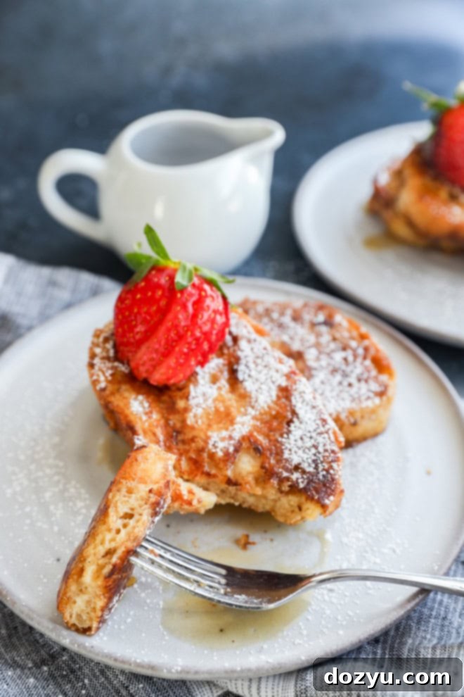 A fork lifts a bite-sized piece of sourdough French toast from a plate, revealing its soft, custardy interior and golden crust, inviting a taste.