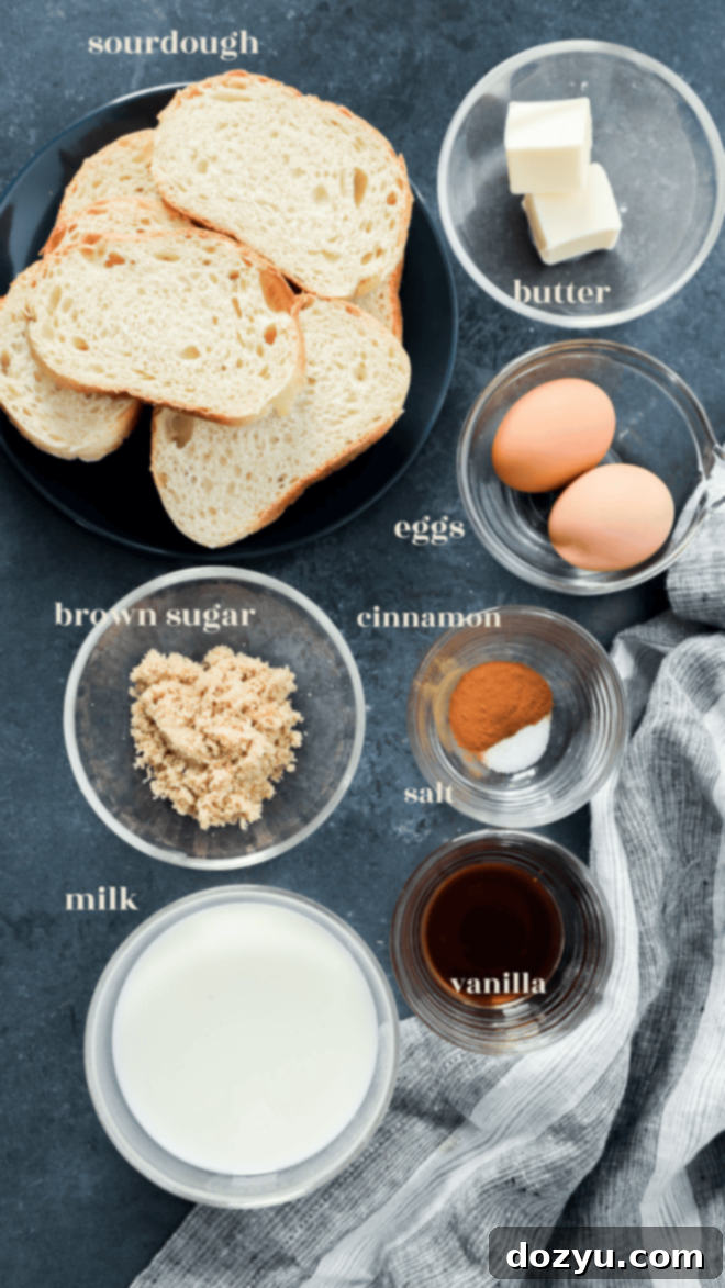 Various ingredients for sourdough French toast are displayed in small white bowls on a wooden surface, including eggs, milk, cinnamon, sugar, vanilla extract, and slices of sourdough bread.