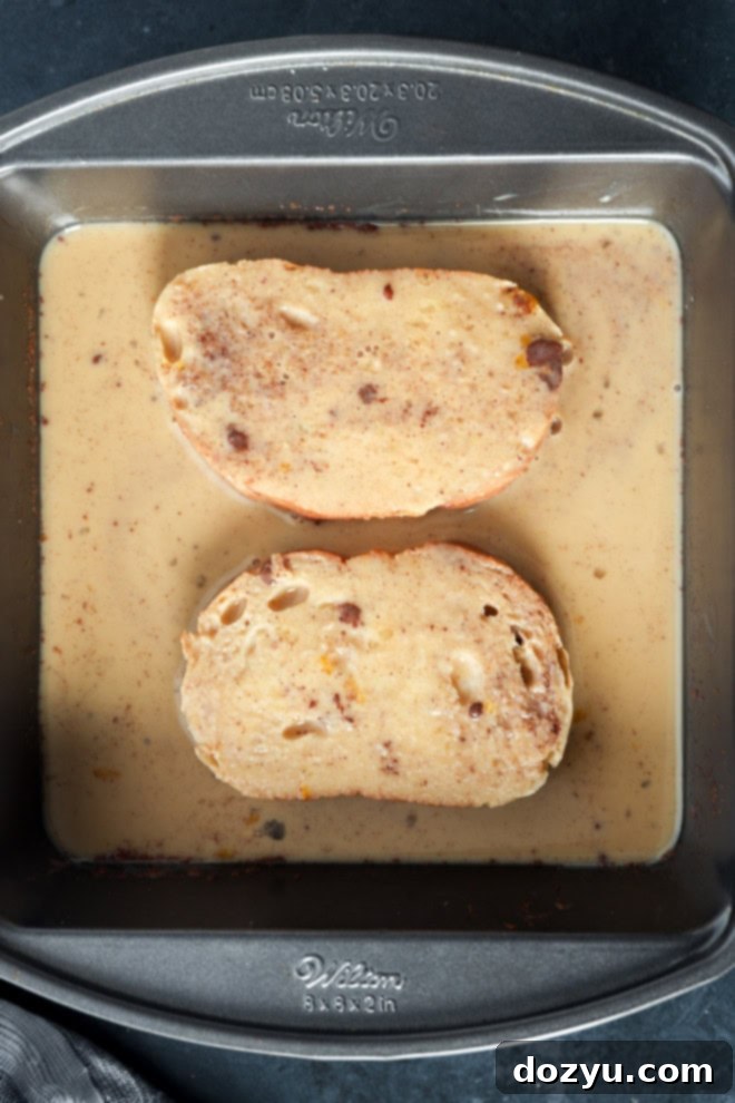 Close-up shot of sourdough bread slices absorbing a spiced egg custard in a shallow dish, highlighting the texture and moisture absorption of the bread as it prepares for frying.